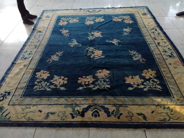 Blue field rug with floral motifs and a pale gold patterned border lying on glossy white tile floor.