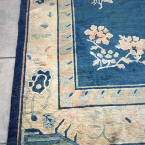 Blue rug with pink and cream floral patterns, featuring a wide patterned border on gray tile.