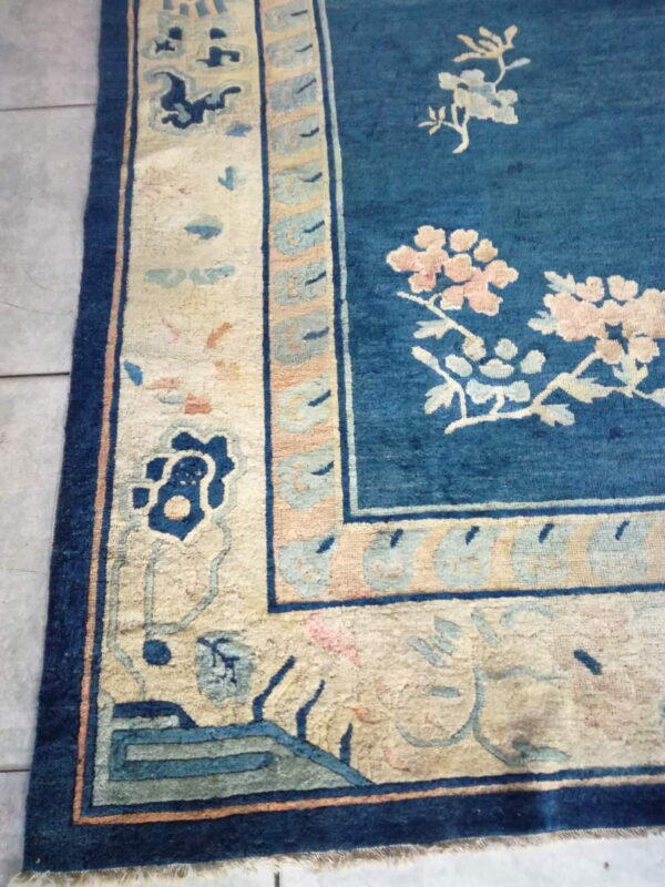 Blue rug with pink and cream floral patterns, featuring a wide patterned border on gray tile.
