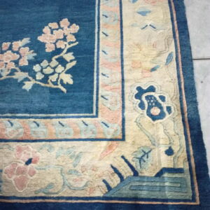 Blue and beige floral bordered rug displaying medium pile texture placed on light gray square tiles.