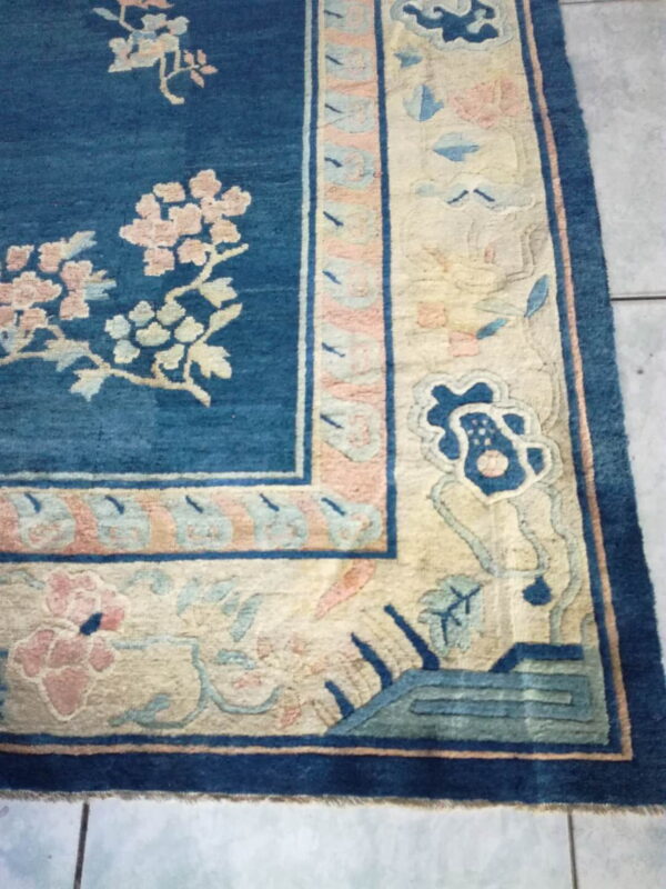 Blue and beige floral bordered rug displaying medium pile texture placed on light gray square tiles.