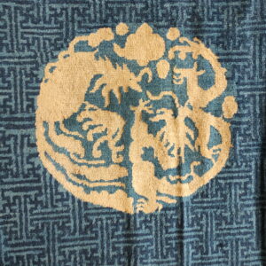 Blue rug detail featuring a light beige medallion showing stylized animals and clouds over a geometric fretwork pattern.