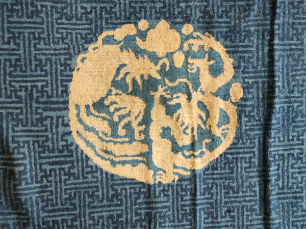 Blue rug detail featuring a light beige medallion showing stylized animals and clouds over a geometric fretwork pattern.
