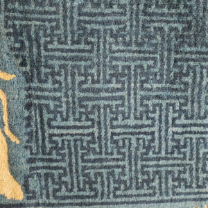 Blue textured rug with a dark geometric pattern contrasting against a large light tan abstract motif.