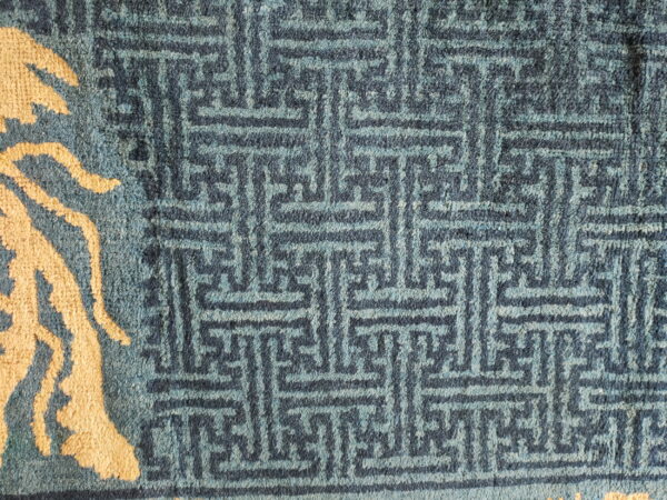 Blue textured rug with a dark geometric pattern contrasting against a large light tan abstract motif.