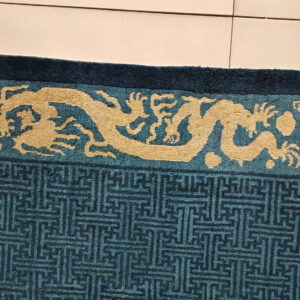 A blue rug detail with a pale gold dragon border and teal geometric patterns rests on beige tile.