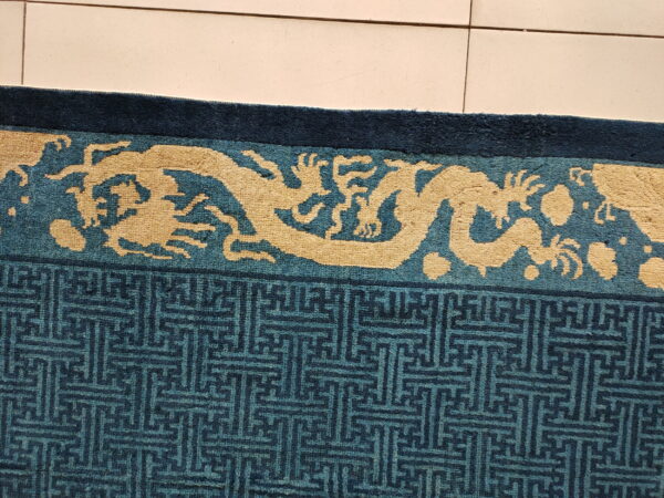 A blue rug detail with a pale gold dragon border and teal geometric patterns rests on beige tile.