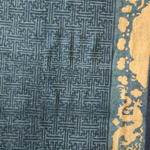 Blue rug with geometric patterning in the field and a yellow border featuring stylized dragon shapes.