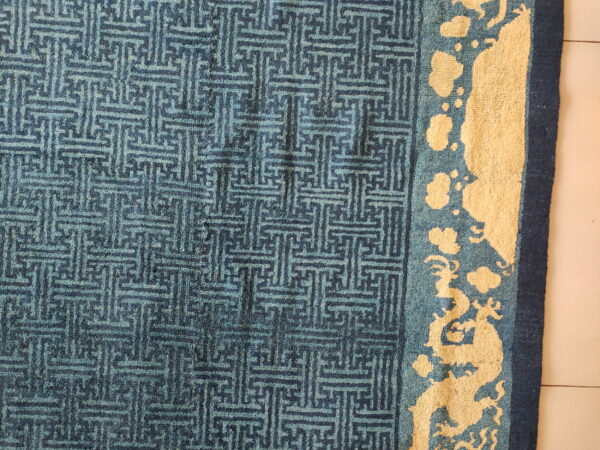 Blue rug with geometric patterning in the field and a yellow border featuring stylized dragon shapes.