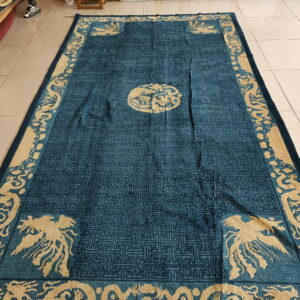Plush teal rug with detailed tan mythological creatures and a dark geometric field pattern on tile flooring.