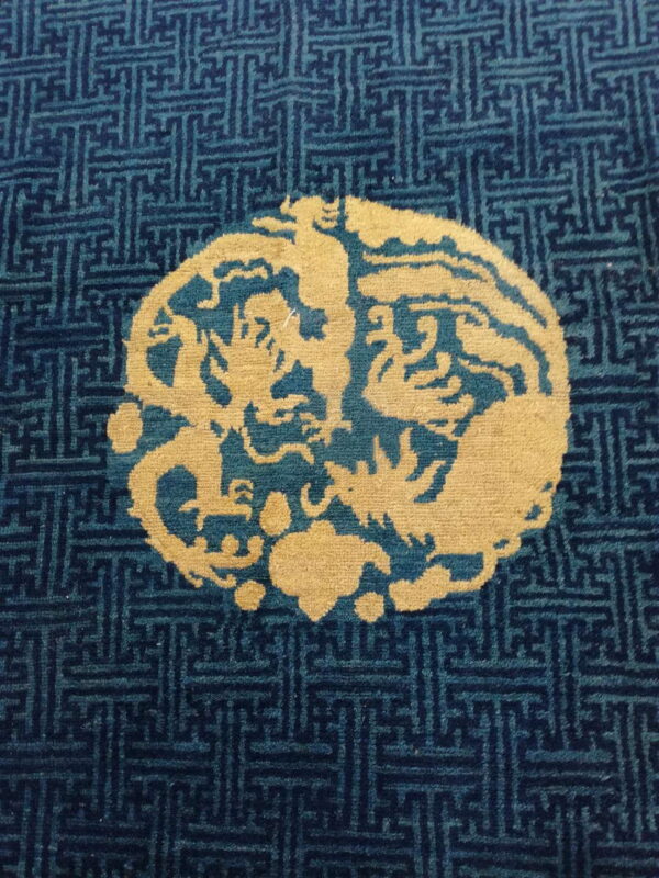 Blue repeating fretwork rug background with a gold oval medallion featuring stylized creatures.