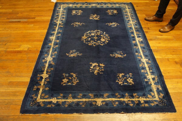 Deep blue rug with scattered gold floral motifs and an elaborate border on wood planks.