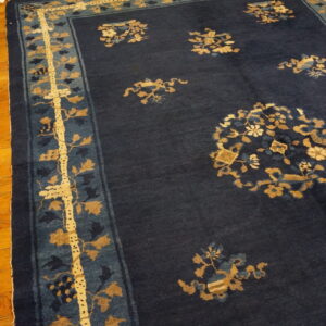 Dark blue rug with gold and light blue floral patterns and a wide border on wood planks.