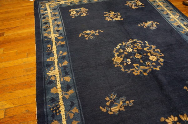 Dark blue rug with gold and light blue floral patterns and a wide border on wood planks.