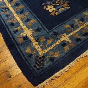 Blue rug with gold and brown floral border pattern on distressed wood planks.