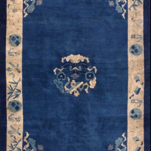 Blue rug with beige border featuring traditional blue and tan motifs lying on wooden floorboards.