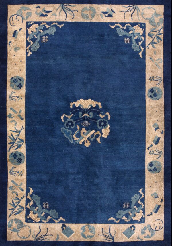 Blue rug with beige border featuring traditional blue and tan motifs lying on wooden floorboards.