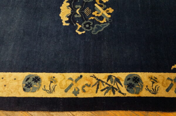 Dark blue high-pile rug featuring gold and teal floral patterns along a thick border on a wood floor.