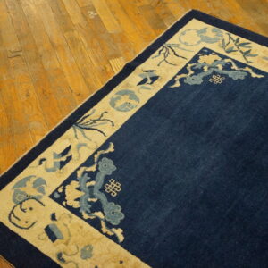 Navy blue rug with patterned beige border lays on warm tone wood planks.