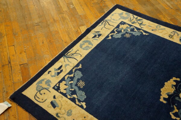Navy blue rug with patterned beige border lays on warm tone wood planks.