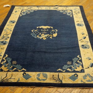 Dark blue rug with a wide light yellow patterned border on a rustic hardwood floor.