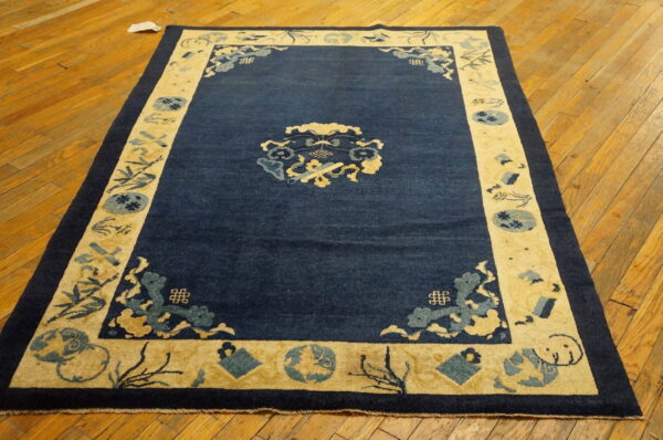 Dark blue rug with a wide light yellow patterned border on a rustic hardwood floor.