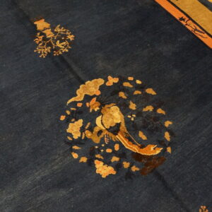 Navy rug with central gold and orange floral bird motif and detailed border on wood floor.