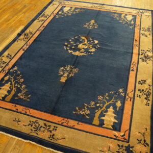 Blue rug with gold and peach pagoda and floral motifs sits on light hardwood floorboards.