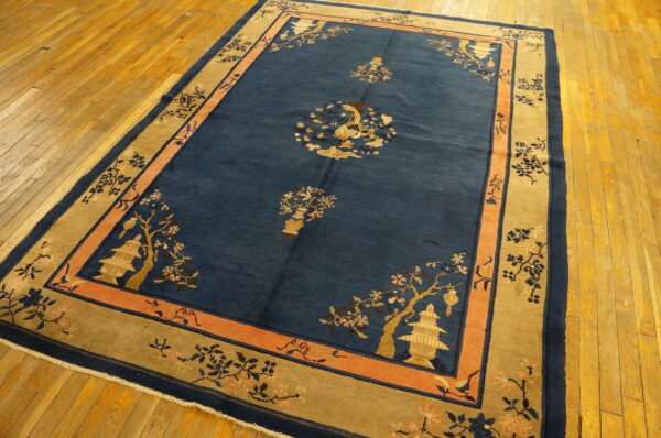 Blue rug with gold and peach pagoda and floral motifs sits on light hardwood floorboards.