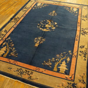 Deep blue rug with tan and coral borders displays stylized floral and pagoda designs on wood flooring.