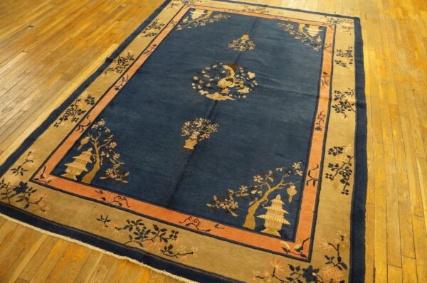 Deep blue rug with tan and coral borders displays stylized floral and pagoda designs on wood flooring.