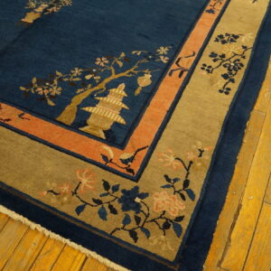 Deep blue rug with gold pagoda motif, flanked by coral and khaki borders on wood floor.