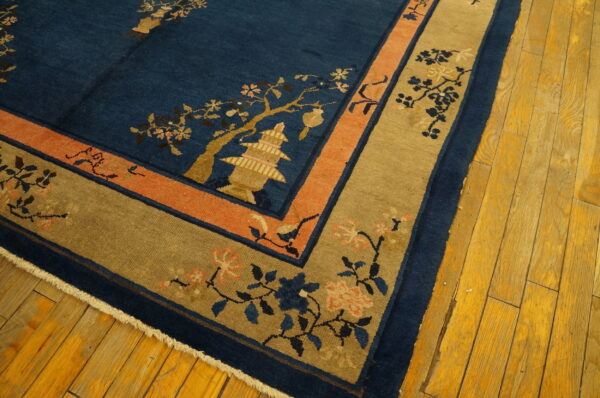 Deep blue rug with gold pagoda motif, flanked by coral and khaki borders on wood floor.