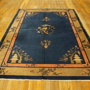 Navy rug with tan and peach borders featuring floral branches and pagodas rests on a polished wooden floor.