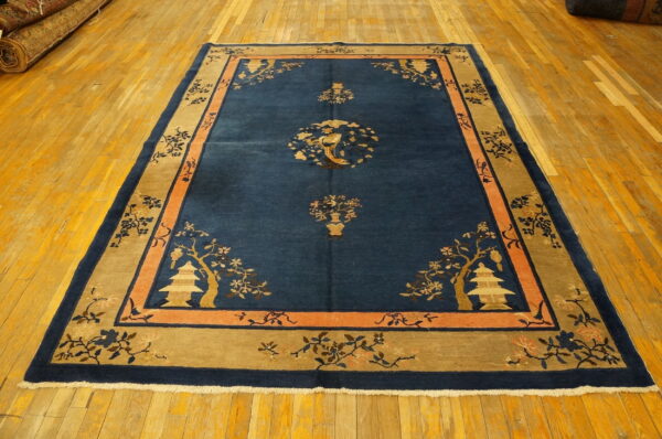 Navy rug with tan and peach borders featuring floral branches and pagodas rests on a polished wooden floor.