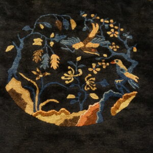 Close-up of a dark navy rug featuring a circular medallion with birds, blue branches, and gold flowers.