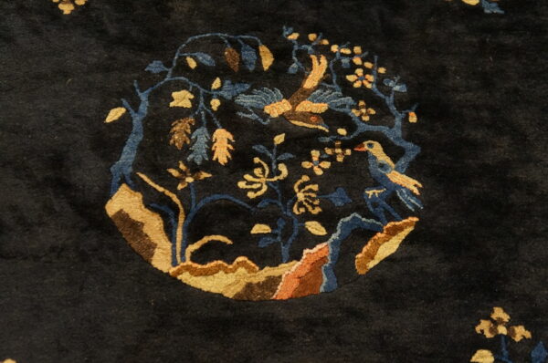 Close-up of a dark navy rug featuring a circular medallion with birds, blue branches, and gold flowers.