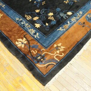 Dark blue rug corner with gold and blue floral patterns, a brown border, and white fringe on wood planks.