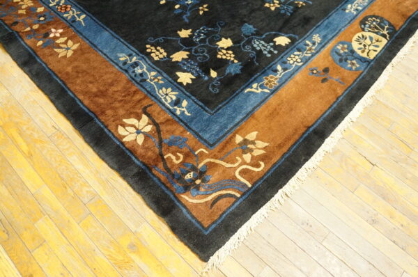Dark blue rug corner with gold and blue floral patterns, a brown border, and white fringe on wood planks.