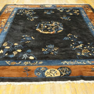 Large black rug featuring blue and beige floral patterns and a wide rust and blue decorative border on wood flooring.