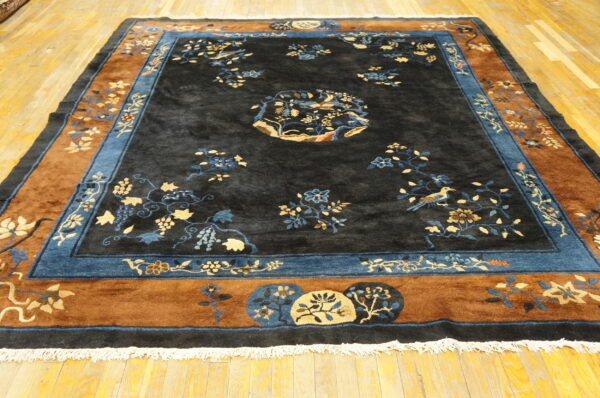 Large black rug featuring blue and beige floral patterns and a wide rust and blue decorative border on wood flooring.