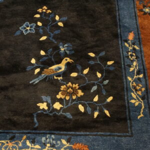 Dark pile rug featuring a gold and blue bird design, surrounded by a striped blue and rust border.