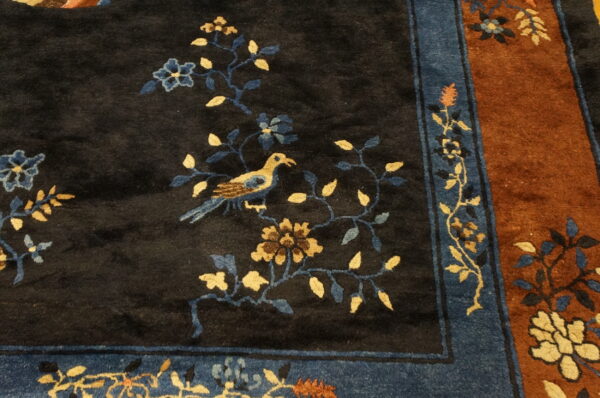 Dark pile rug featuring a gold and blue bird design, surrounded by a striped blue and rust border.