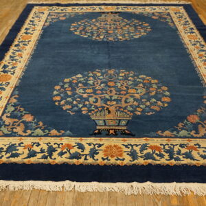 Deep blue rug features two vase-and-tree motifs and a detailed floral border over distressed wood floors.