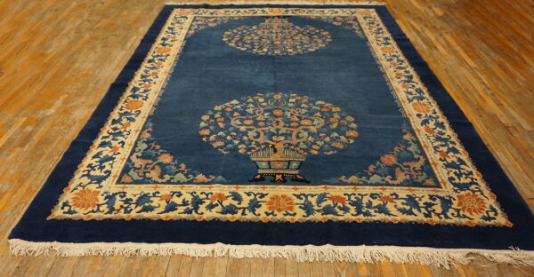 Deep blue rug features two vase-and-tree motifs and a detailed floral border over distressed wood floors.