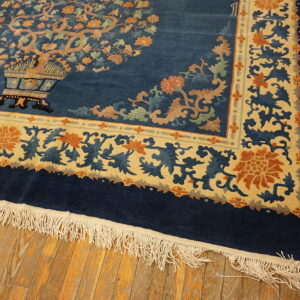 Navy blue rug with a tan floral border and vase pattern rests on rustic wooden plank floors.
