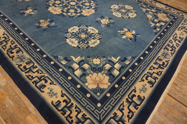 Blue rug with cream floral medallions and complex borders rests on wide plank wooden floors.