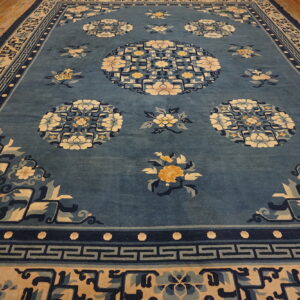 Medium blue rug with cream and gold floral medallions and intricate geometric borders on a wood floor.