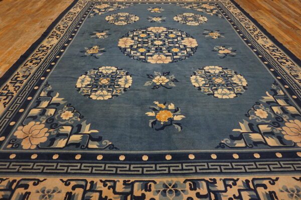 Medium blue rug with cream and gold floral medallions and intricate geometric borders on a wood floor.