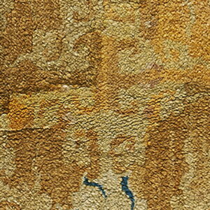 Textured gold rug detail showing large floral motifs and small accents of dark blue.
